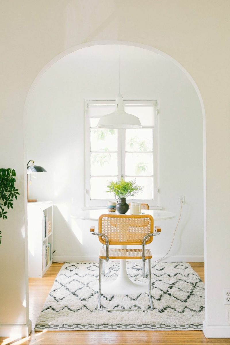 A room with white walls and a polished wooden floor. In the center, there is a simple table and a chair. The room appears clean and minimalistic.