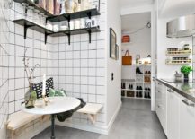 A small kitchen with white tile walls and shelves. Wall-mounted bench seats with a round table.