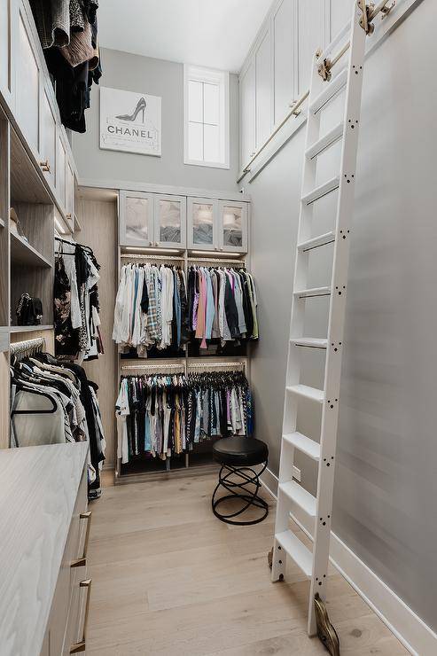 Walk in closet features a white ladder on rails and gray shelves under a tall ceiling