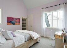 In this beautiful lilac girl's bedroom, a stained oak bed is dressed in purple and gray bedding and faces a window framed by a lilac wall and covered in sheer white curtains. To the side of the bed, a lucite z-chair sits at a mirrored desk placed on gray carpeting.