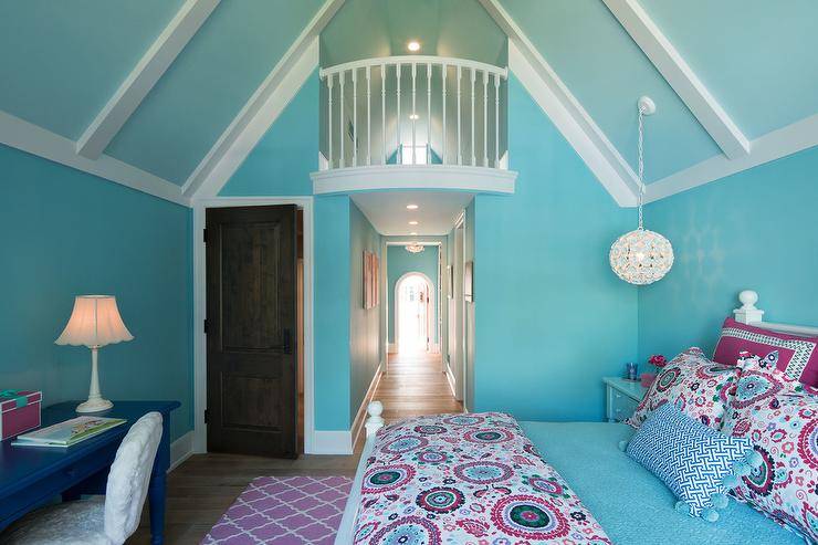 Welcoming blue and pink girl's bedroom features a white wood bed dressed in pink and blue suzani style bedding accented with a blue lumbar pillow placed in front of pink and blue suzani style shams. A white flower light hangs from a blue vaulted ceiling above a blue nightstand positioned against a blue wall. A pink trellis rug sits in front of the bed and behind a white faux fur chair placed at a blue desk.