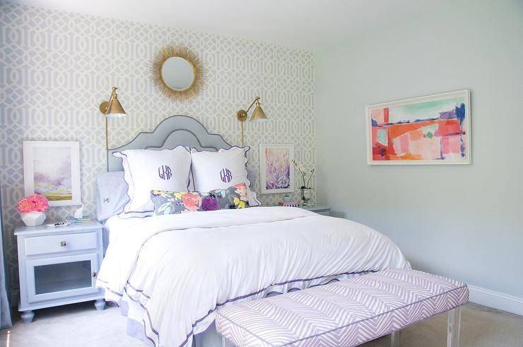 Soft pastel colors and a classic style will keep this girls room timeless. Trellis wallpaper walls with gold accented mirror and Boston Functional Library Wall Lights create a chic vibe across the wall and allow a curved purple headboard and monogrammed bedding to be the center of attention. Blue nightstands are decorated with floral arrangements and accessories while framed wall art is featured over them. A purple zebra bench with lucite legs is seated at the end of this luxe bed adding a dimensional and fun pattern!