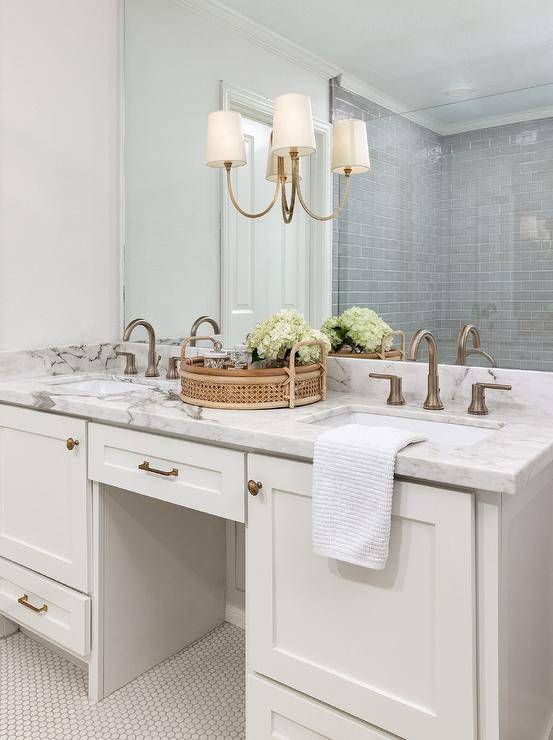 Brass hardware complements a white shaker washstand donning a marble countertop and dark nickel faucets fixed beneath a frameless vanity mirror finished with a Reed Double Sconce.