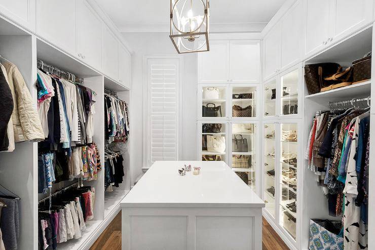 Spacious custom walk in closet features lighted purse cabinets and a white island.