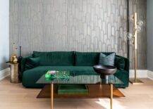 Chic Speakeasy Wallpaper covers an accent wall complementing blue walls and fixed behind an emerald green velvet sofa matched with a round brass end table and a black glass and brass coffee table.