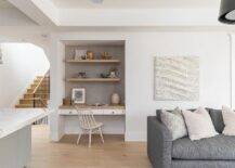 Wood floating shelves are mounted against taupe wallpaper and over a two-tone built-in desk paired with an off-white spindle chair.