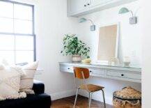 Cozy family room features a vintage wood and metal desk chair placed at a light gray floating desk fitted with drawers donning oil rubbed bronze knobs and fixed beneath green glass task lights mounted under gray cabinets.