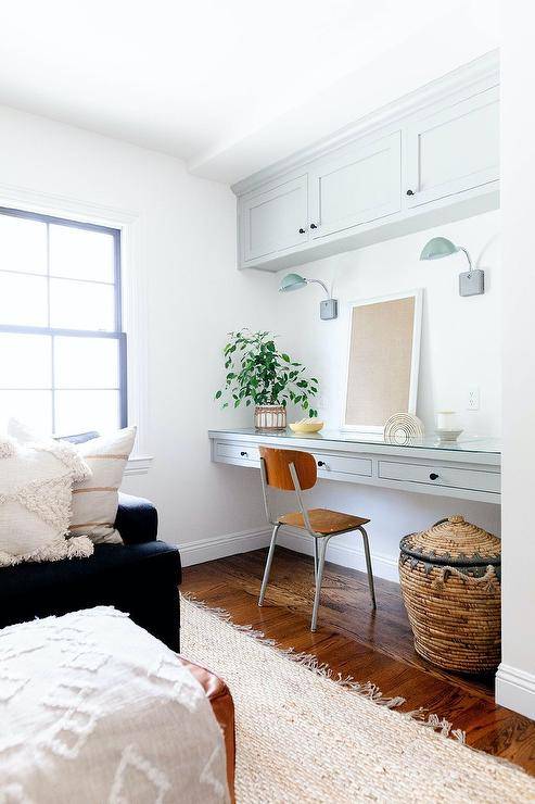 Cozy family room features a vintage wood and metal desk chair placed at a light gray floating desk fitted with drawers donning oil rubbed bronze knobs and fixed beneath green glass task lights mounted under gray cabinets.