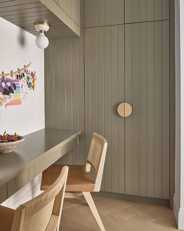 White and gold mini flush mounts mounted under green plank cabinets light a green plank built-in desk matched with cane and leather chairs. Stacked green plank cabinet are inset into a green plank wall.