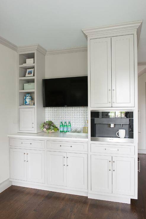 Kitchen coffee station features white cabinets with glass and nickel pulls, a built-in Miele coffee maker with trim and a mounted TV.