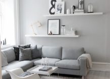 Modern living room with two white floating shelves featuring a lamp, pictures, and glass containers.