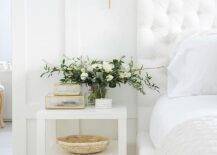 White master bedroom design features a white velvet tufted headboard with a white nightstand and a brass sconce for a warm sophisticated finishing touch.