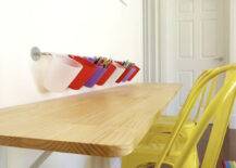 Kids' playroom with long wall mounted wooden desk lined with kid sized yellow Tabouret chairs with wall mounted pencil holders above.