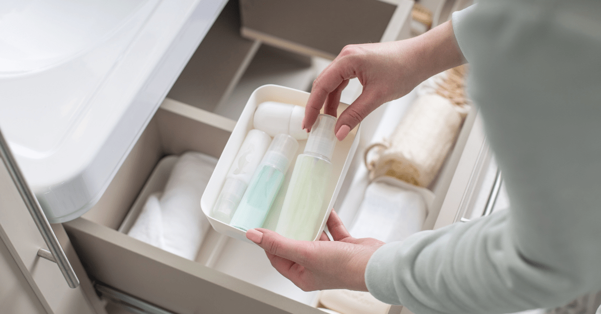 Closeup of someone's hands grabbing a spray bottle from a bathroom drawer organizer.