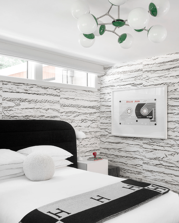 Black and white modern boy's room features a black channel tufted headboard accented with a black Hermes throw blanket and white ball boucle pillow and a white nighstand on black and white wallpaper.