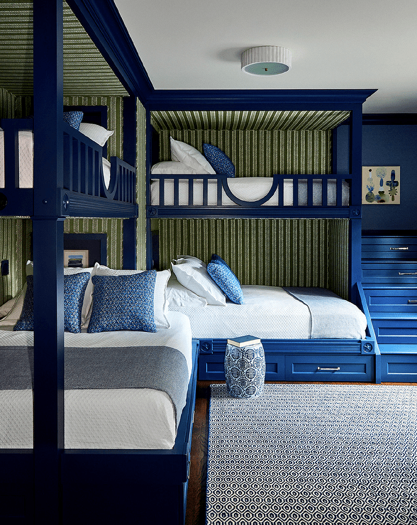 Bedroom features blue L-shaped built in bunk beds with blue built in staircase, green striped wallpaper and a blue rug.