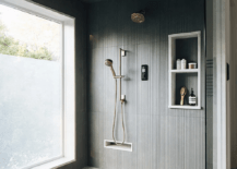 Large walk-in shower boasts a glass partition and a teak slatted floor, as black striped wall tiles frame stacked niches fixed beside a satin nickel shower kit under a black striped ceiling.