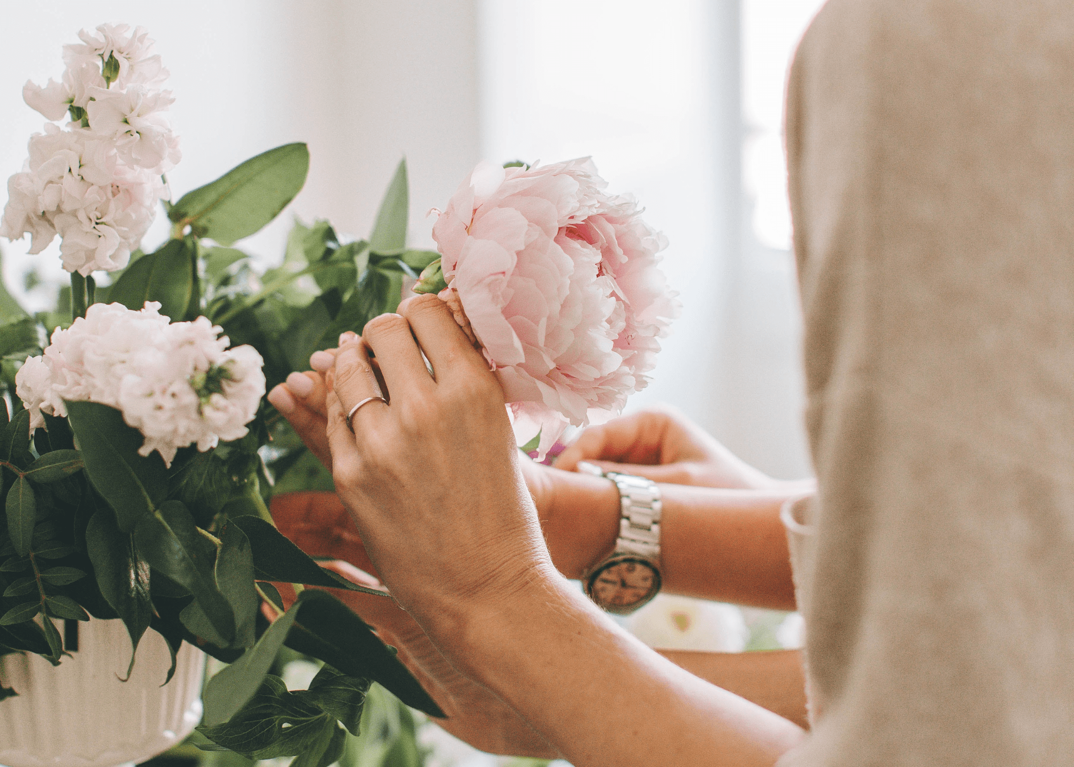 woman placing a pink peony in a flower arrangement