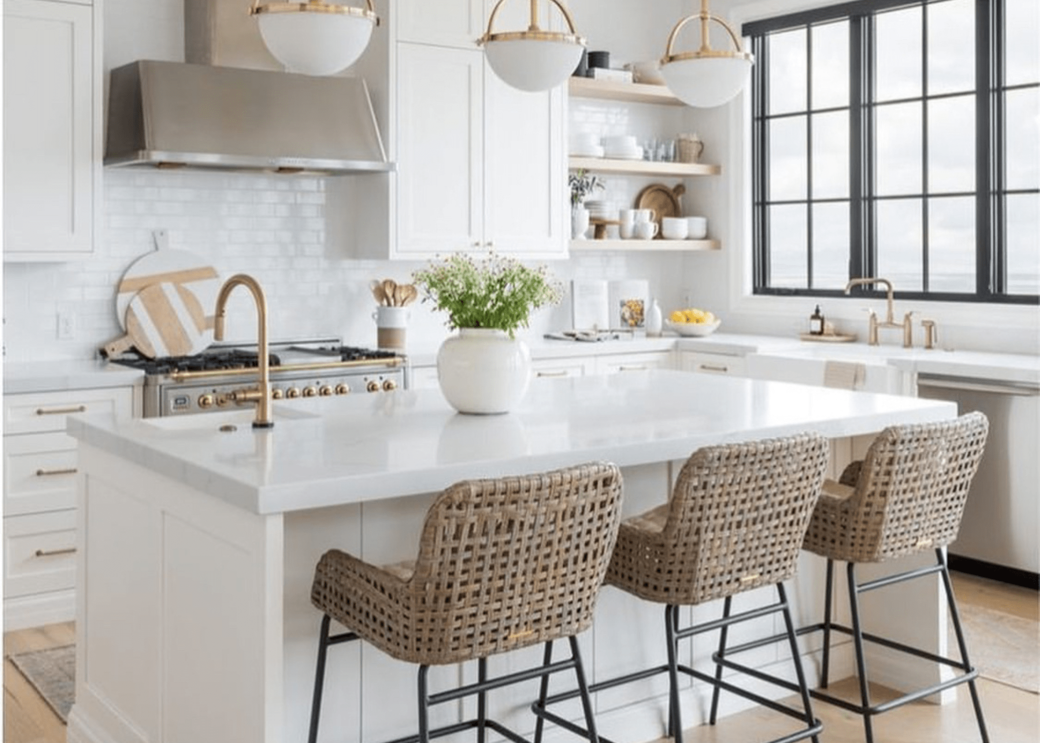 white kitchen with island and bar stools gold fixtures and stainless steel stove and hood