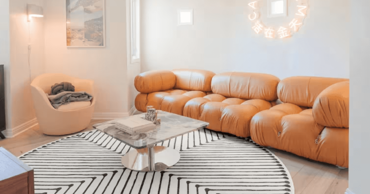 A round rug in living room with brown leather coach.